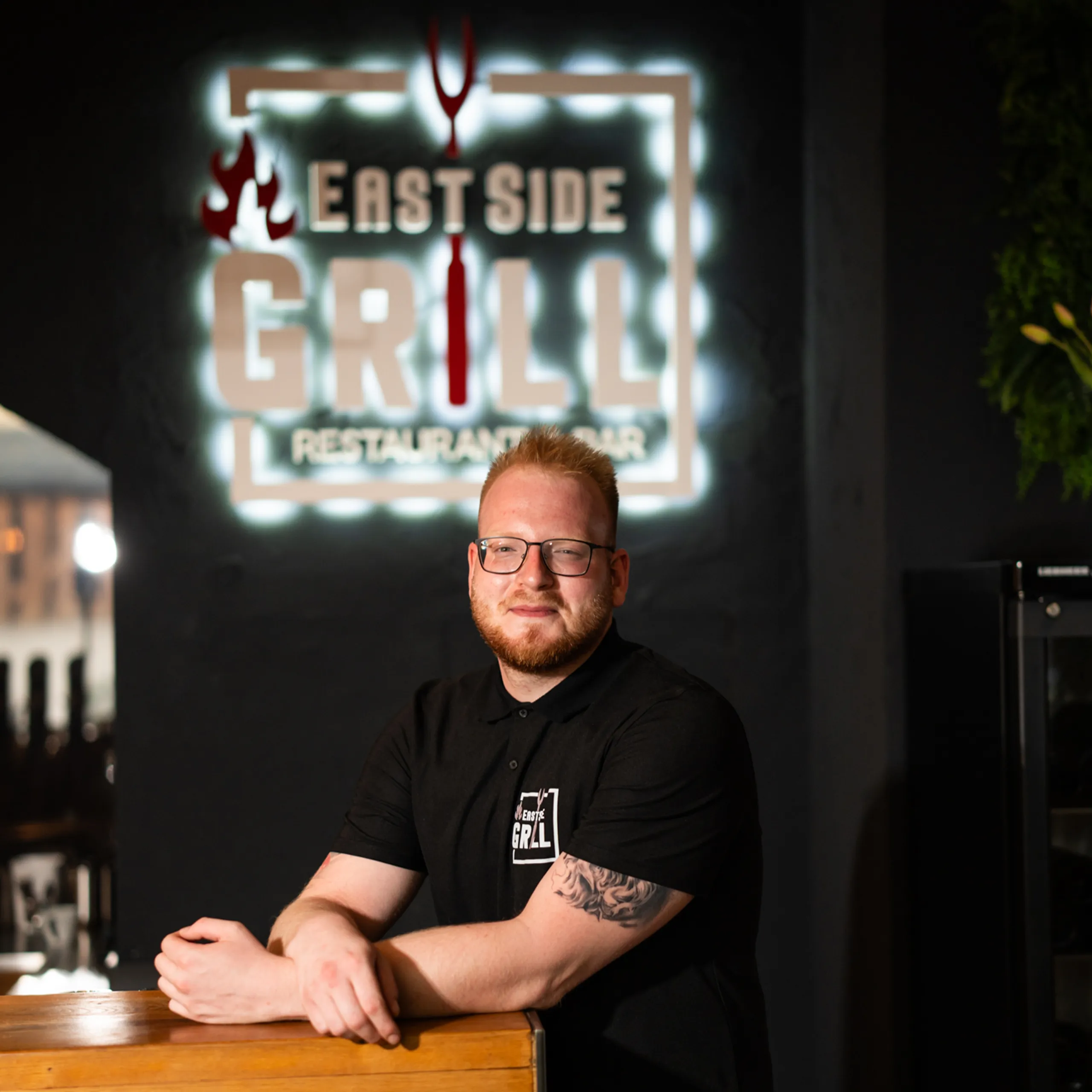 Branko Vujanovic, Chefkoch und Geschäftsführer des EastSide Grill, im Restaurant vor dem beleuchteten Logo Branko Vujanovic, Chefkoch und Geschäftsführer des EastSide Grill, im Restaurant vor dem beleuchteten Logo