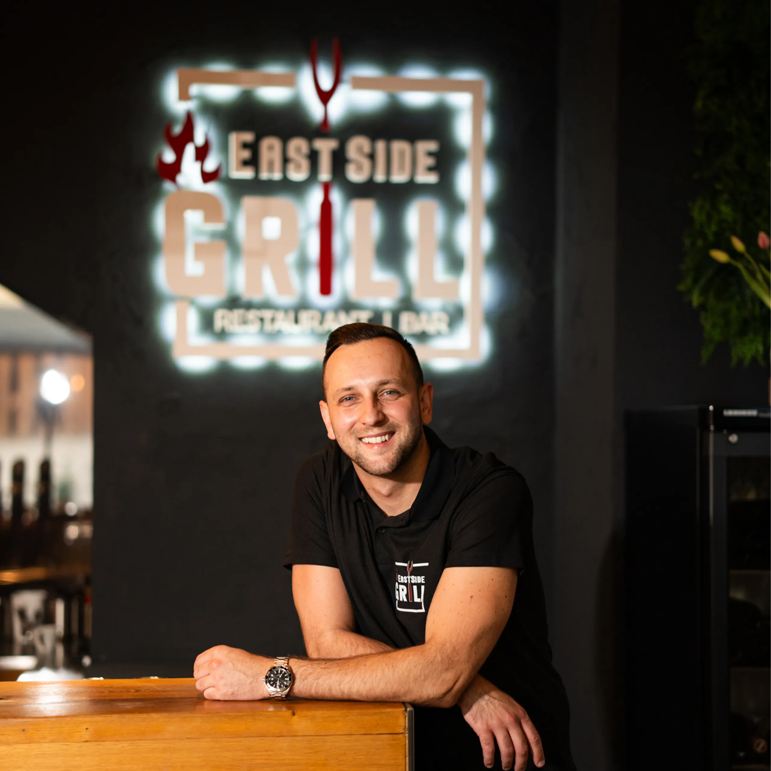 Zeljko Vujanovic, zweiter Inhaber des EastSide Grill, im Restaurant vor dem beleuchteten Logo Zeljko, zweiter Inhaber des EastSide Grill, im Restaurant vor dem beleuchteten Logo